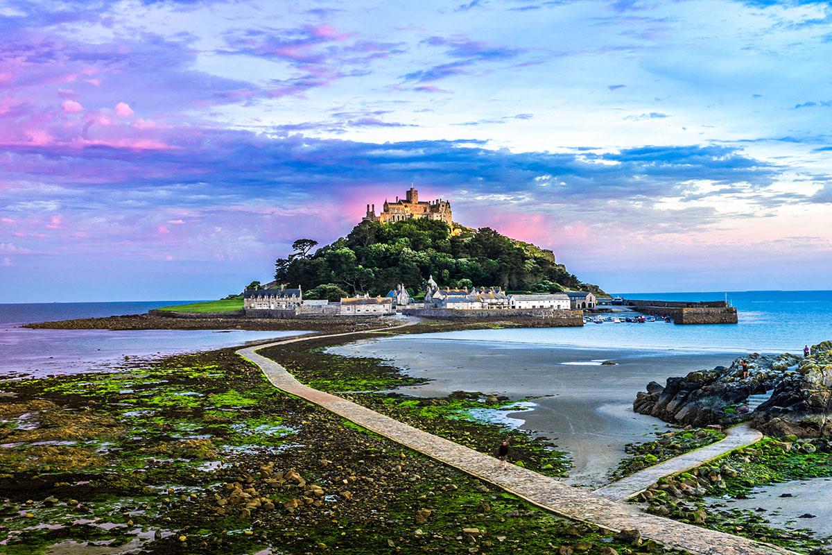 St Michael's Mount, a National Trust property in West Cornwall. Standing from Marazion Beach and looking over the sea. The sunset is in the background.