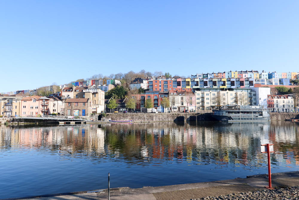 The harbourside at Bristol, with bright blue water and colourful houses in the background.