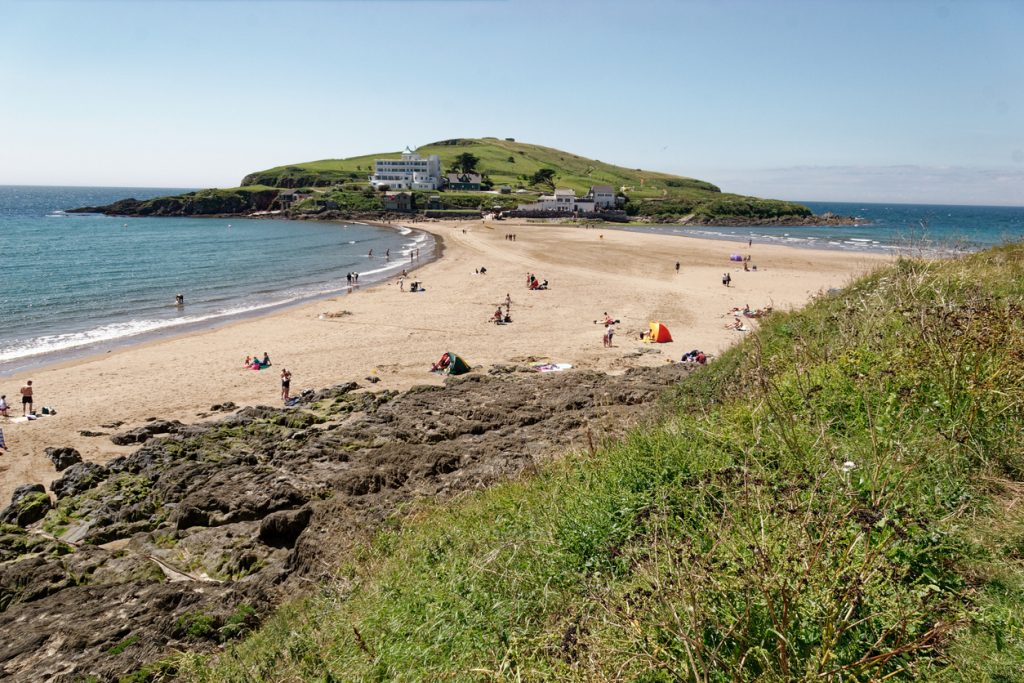 Small seaside village. Golden sands and Burgh island which is cut off from mainland twice a day. Tide is out. Long stretch of sand between mainland and island. Popular bathing beach.  Art Deco hotel on island.