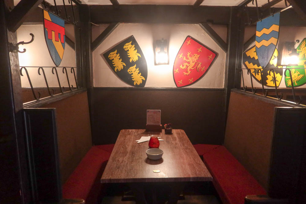 Dark meadery in Cornwall. Meaderies are medieval-themed restaurants dotted around Cornwall. Empty table is in foreground and medieval shields in background.