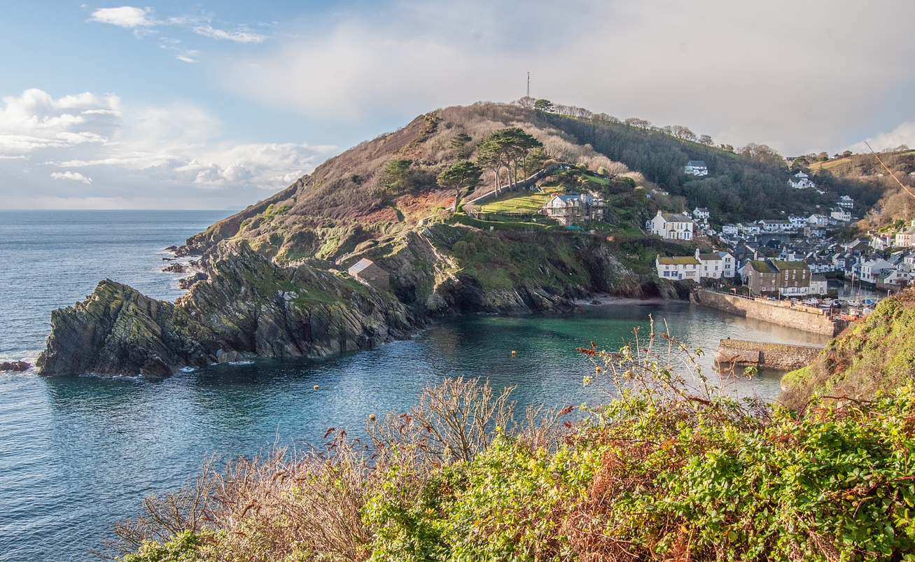 Scenery of Polperro, with big rock in background and beach in foreground. The rock, Chapel Rock, is one of the best hidden gems in Cornwall.