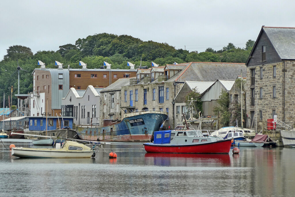 Houses lining the harbour in Penryn, Cornwall. There are boats bobbing along the water. 