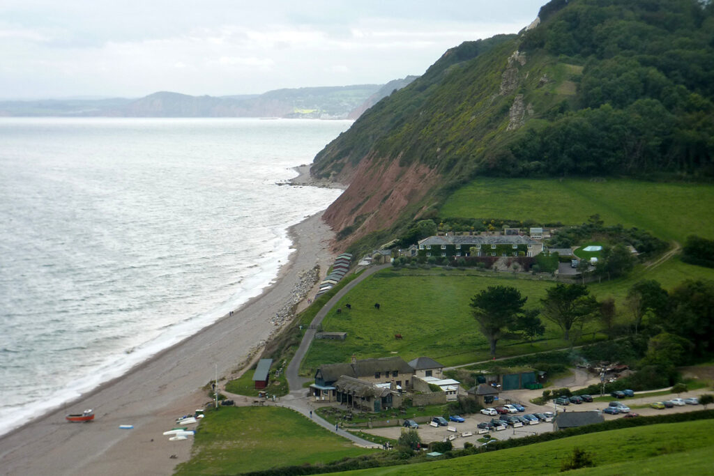 A view of Branscombe Beach from a high point of the cliff. There is a view of the beach, green fields and the sea.