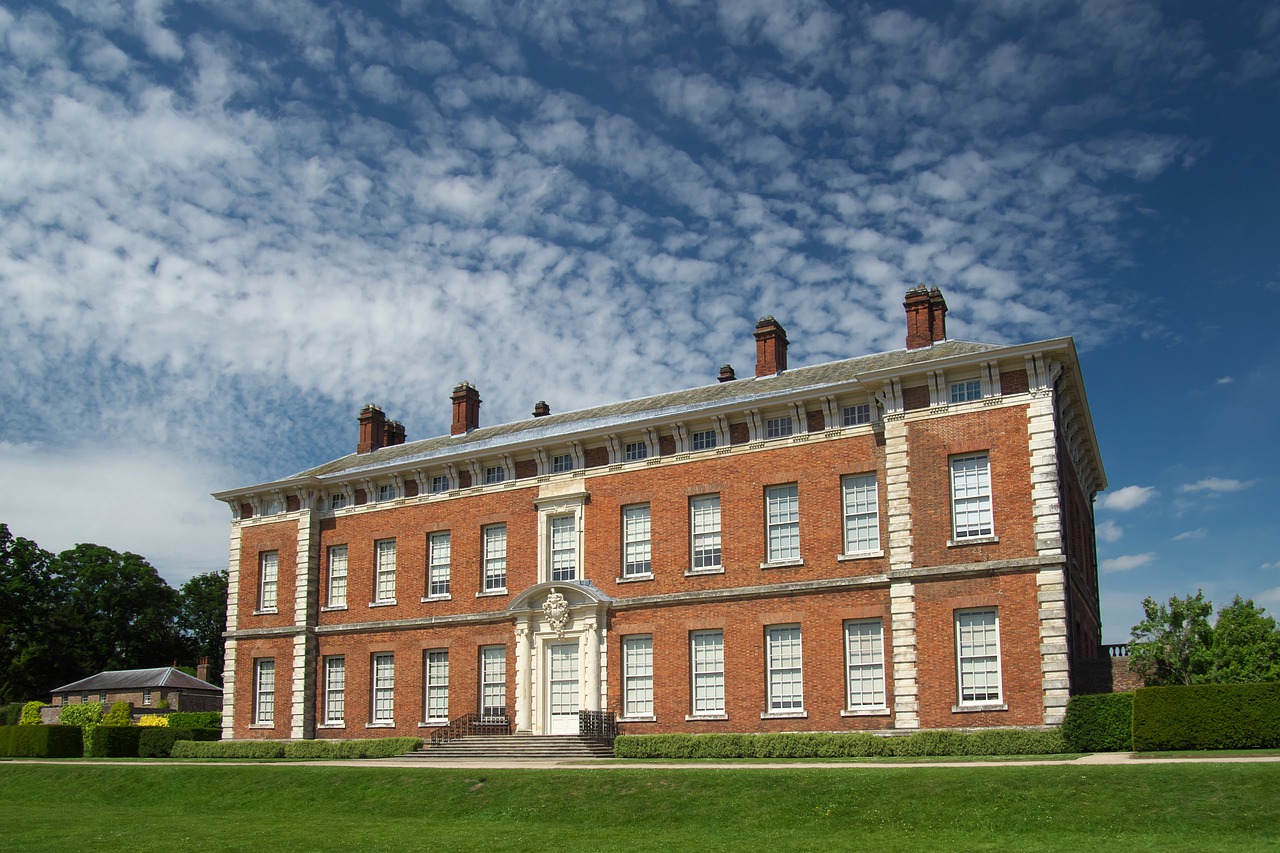 Large historical mansion with terracotta walls and blue sky with light clouds in the background. One of the places you can visit with a National Trust membership!