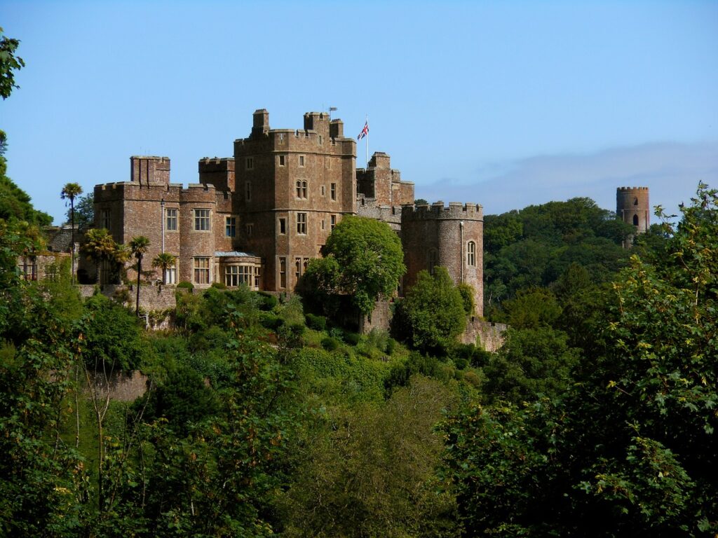 A shot of Dunster Castle, a 1000 year old brick castle sitting on top of a hill in Exmoor, with trees surrouding the base.