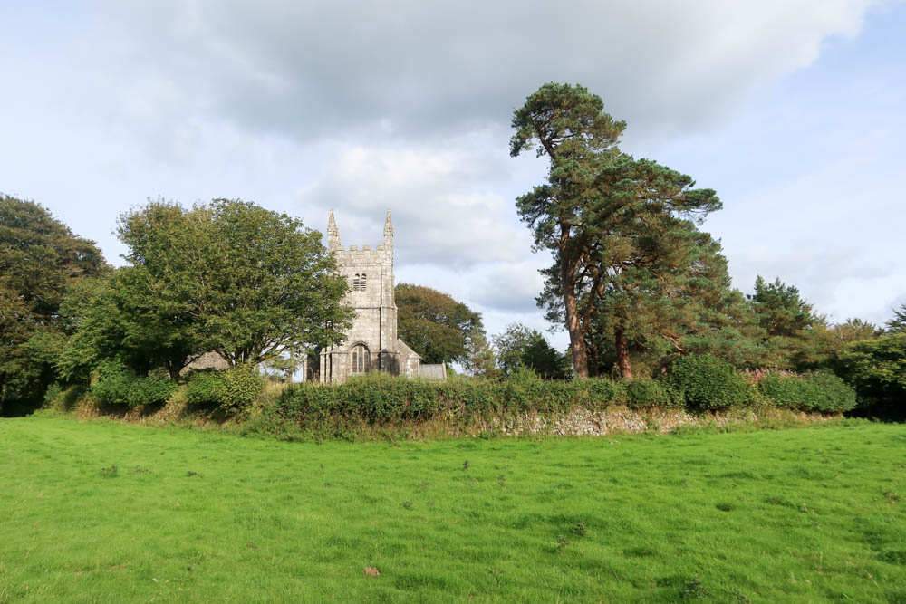 A view of a church and churchyard, with a cloudy sky in the background and grass in the foreground. 
