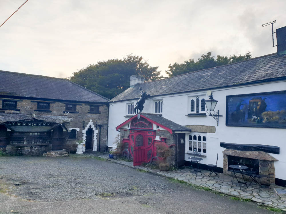 The outdoors of the Highwayman Inn, Britain's most quirky pub near Dartmoor National Park, Devon. There's a pink door in the shape of a carriage and white walls in the background. 