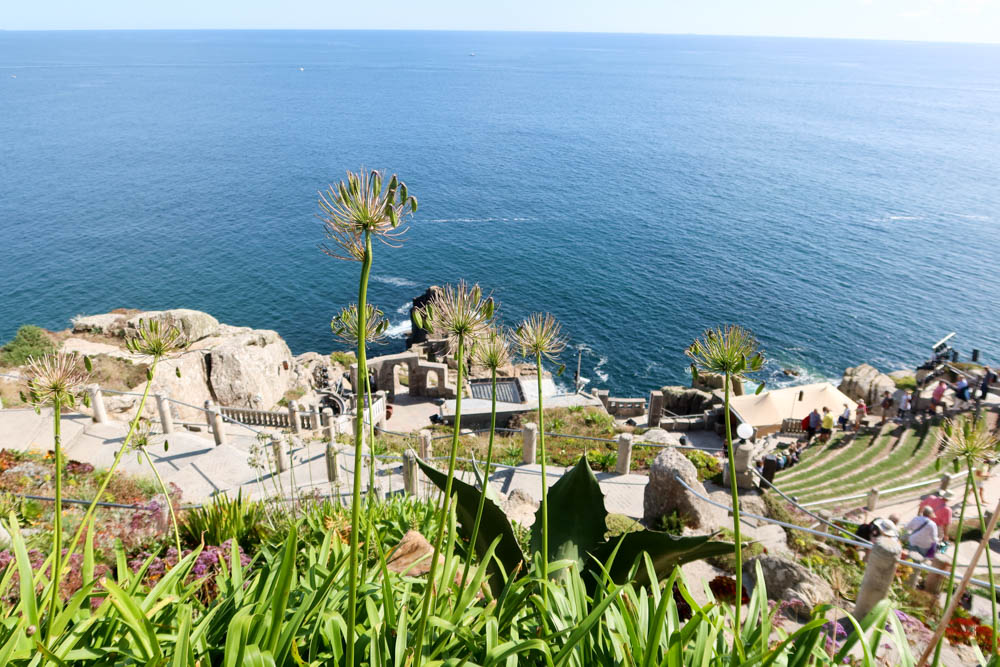 Sub tropical plants are in the foreground with the rocky Minack Theatre, Porthcurno in the background. You can also see the beautiful sea.