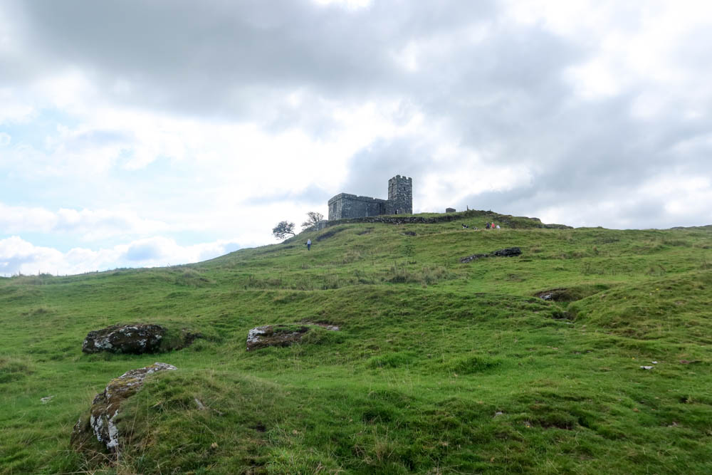 Brent Tor church on the top of a big tor in Dartmoor, Devon. The sky in the background is cloudy and the green class is in the foreground