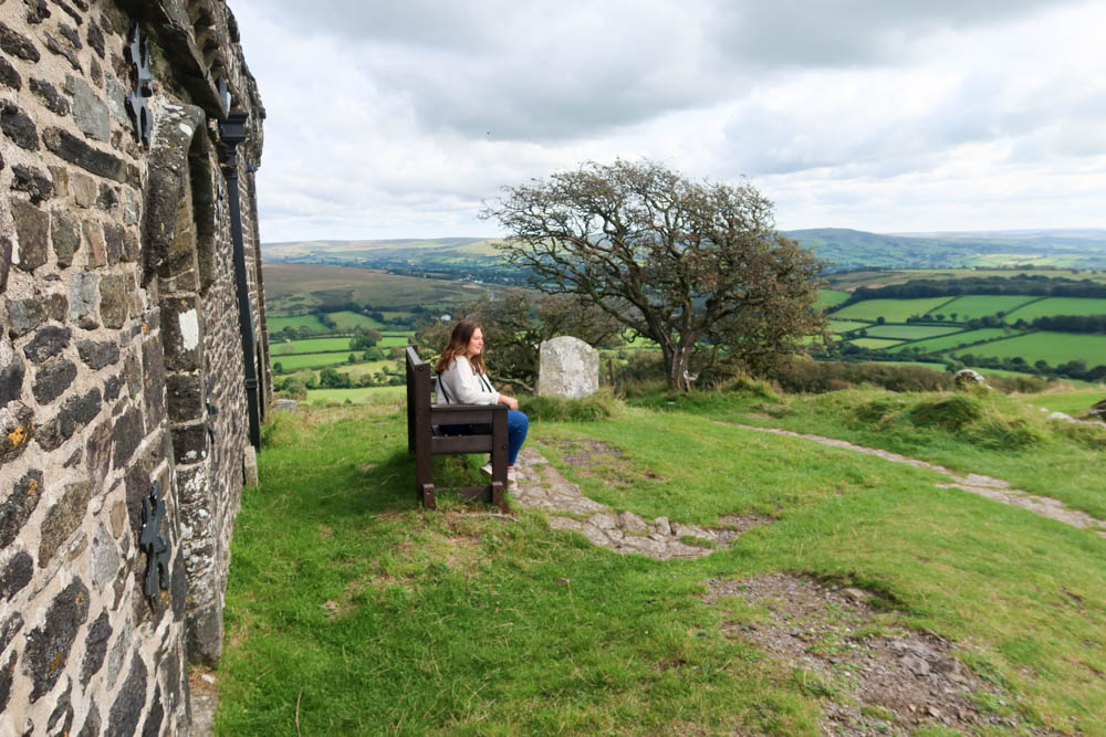 Girl sitting on a bench by a granite wall. There are beautiful fields in the background
