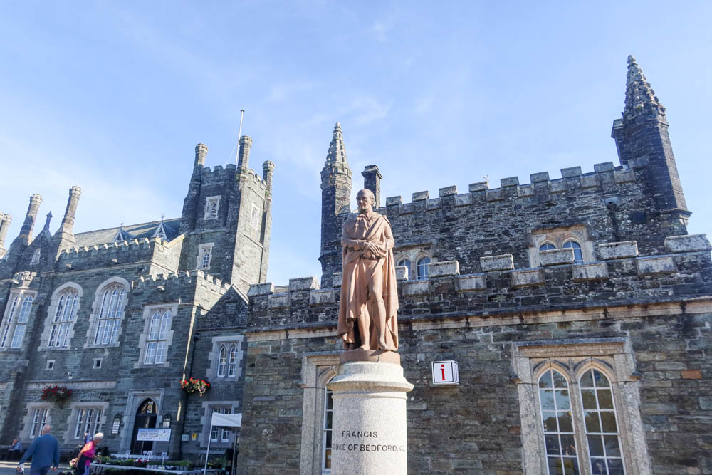Tavistock town hall, with gothic detailing. The sky is blue and a statue of the Duke of Bedford is in the foreground.