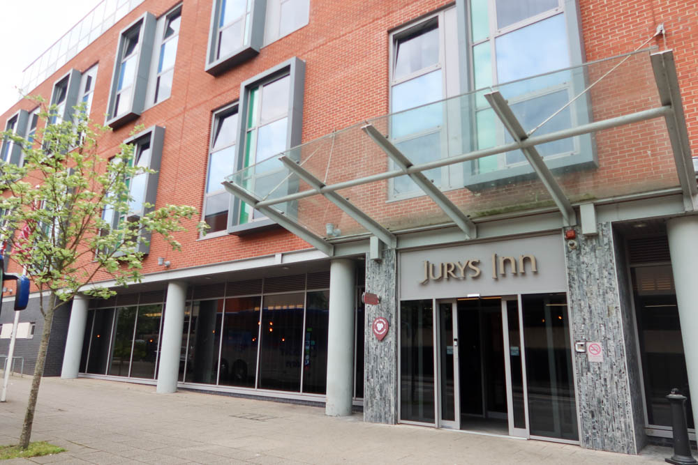 The outside of Jurys Inn in Exeter. There is red brickwork above the entrance and golden lettering of the hotel name. 