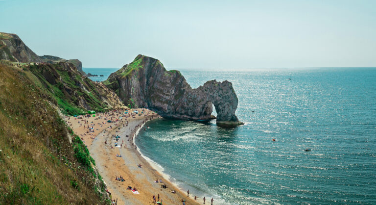 Durdle Door with people relaxing on the beach on a sunny day in August 2020.