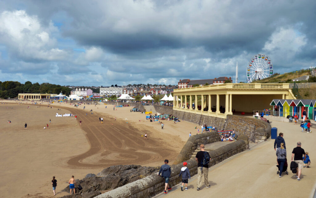 Barry Island, Wales - 6 August 2017: People walking along the promenade with the tracks from a tractor cleaning visible on the beach beach visible