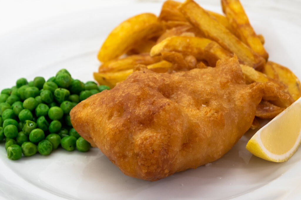 Fish and Chips with Peas and Lemon on a White Plate, a Typical Traditional Dish of English Cuisine with Deep Fried Cod and Fries