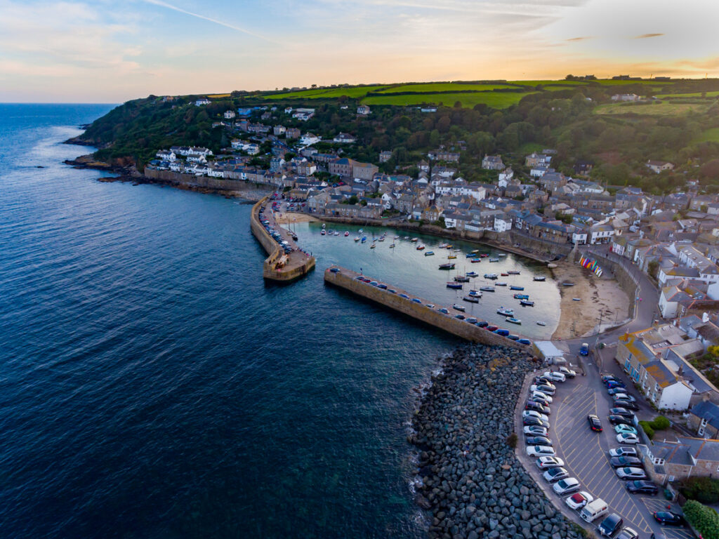 Aerial view of the village of Mousehole. From the vantage point, you can see the sea and harbour, with the village spreading out and fields behind.