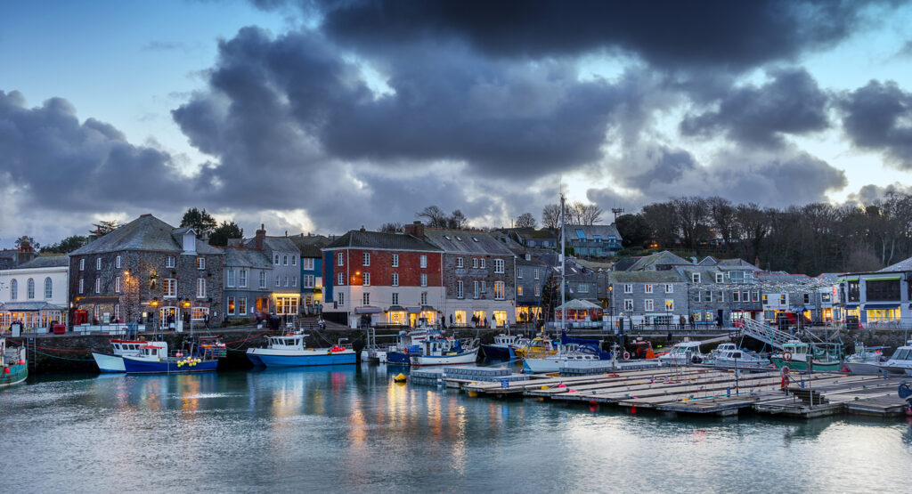 The harbour of Padstow with dark storm clouds hanging over it. You can see the water in the harbour and historical buildings of the town.