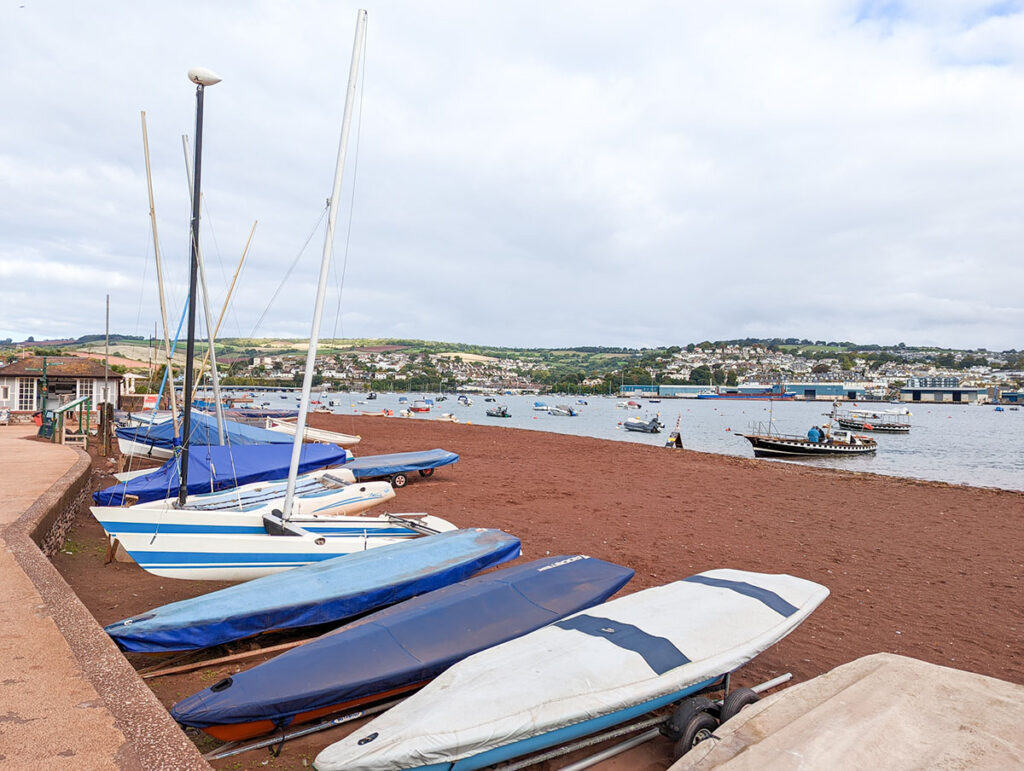 Red sands of Shaldon Beach with boats lining the back. It's river beach, so there are views across to Teignmouth.