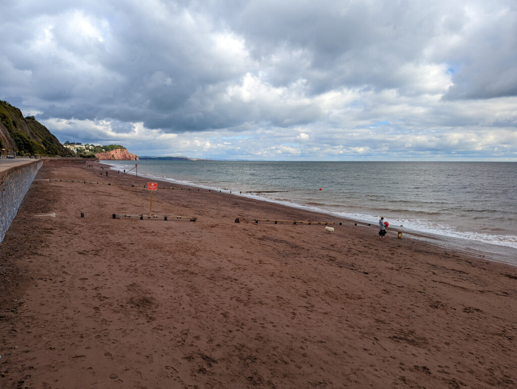 View of the reddish sand at Teignmouth beach. There's a cliff in the background. 