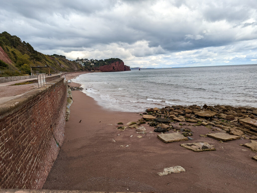 The sands of Teignmouth beach with the sea wall on the left and the sea at the top.