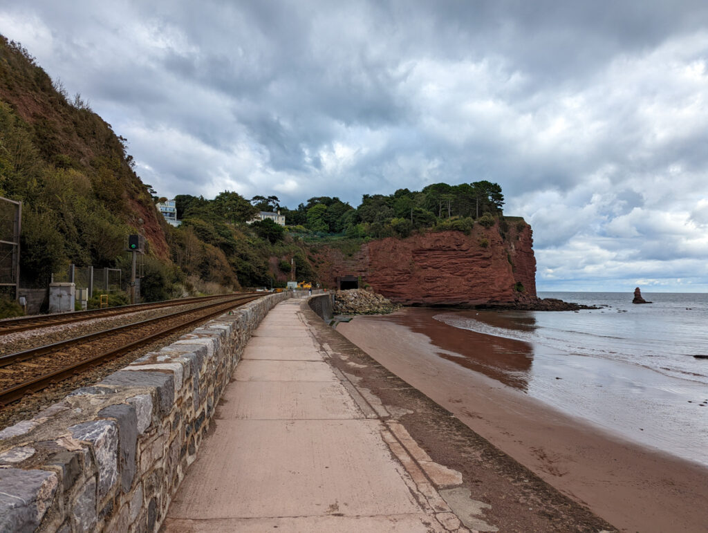 Walk along Teignmouth sea wall, with the railway one side and the sea on the other, and the cliffs in the background