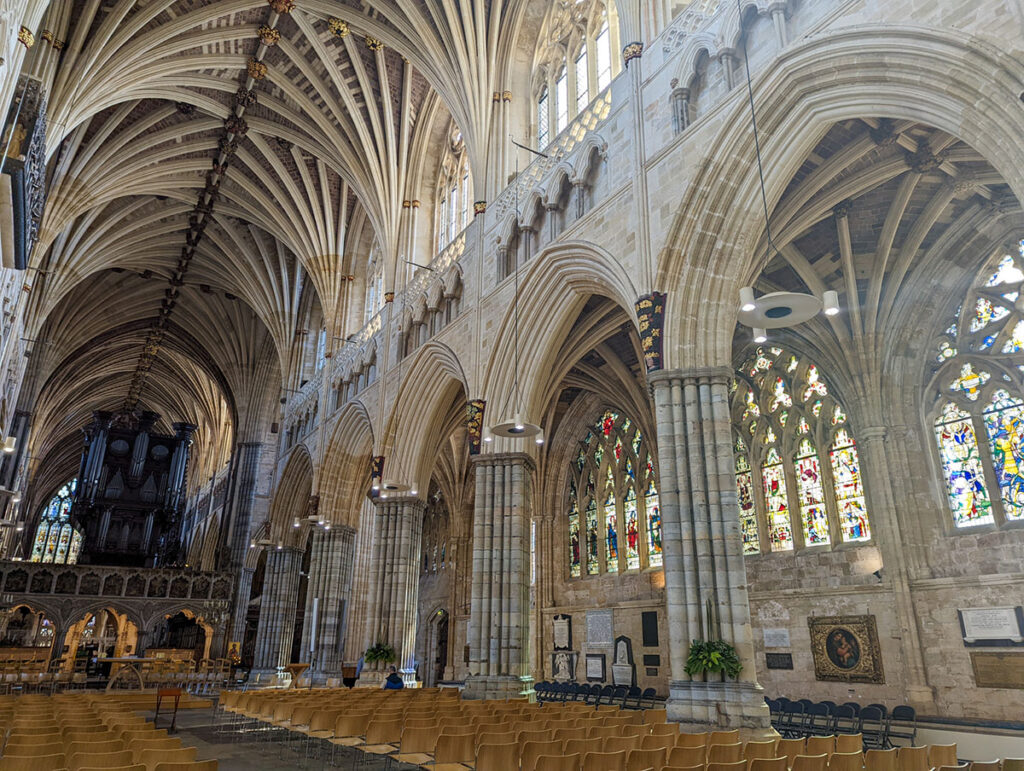 A view of beautiful Exeter Cathedral, with the ribbed vaulting ceiling above and the arches.