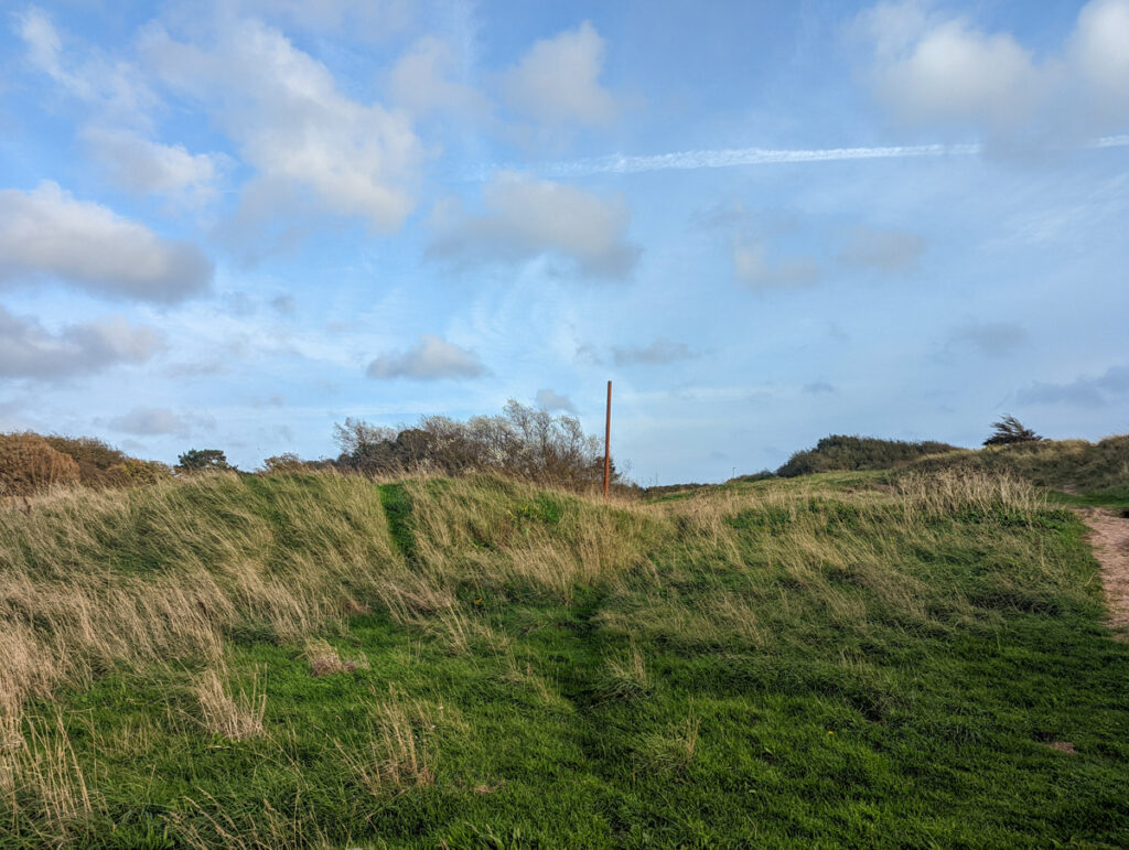 View of the Maer, a grassland in Exmouth, with rusty pole in the background and a sky with light cloud cover