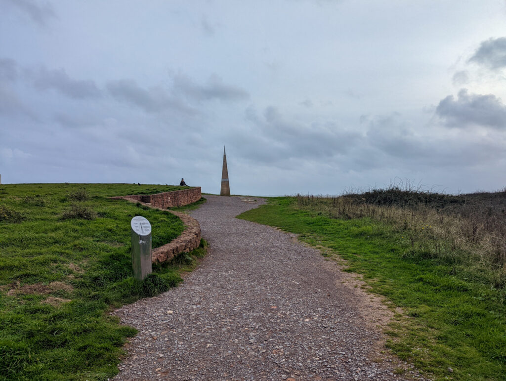 View of Orcombe Point, a triangle shaped monument that's on the eastern end of the Jurassic Coast, with a sign in the foreground. 