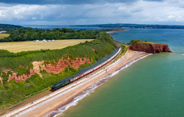 A lovely drone image showcasing a steam train leading the way along the famous Dawlish Sea Wall.