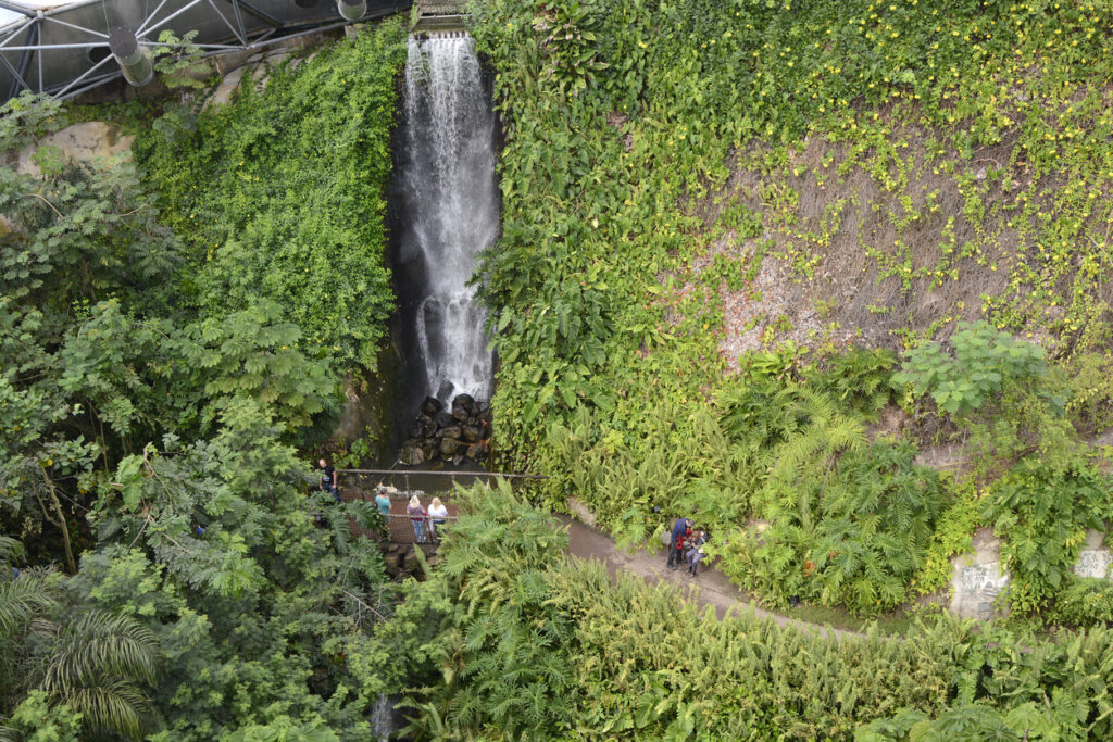 Truro, England - September 14, 2015: Inside the Eden Project Tropical Forest BioDome. Waterfall with people walking by