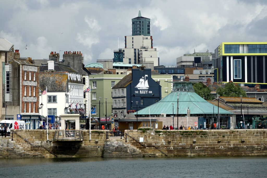 Looking across the marina to The small arch which is the Mayflower steps commemorating the departure of the Pilgrim Fathers to the New World in1620. Views of the city skyline to the rear