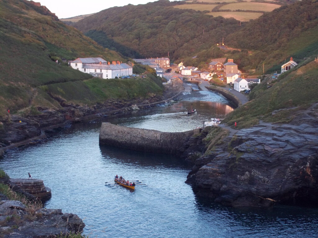 The harbour at Boscastle, with the evening sun about to set, making the sea glow and the boat ride into the harbour. The village and the trees complete the picture.