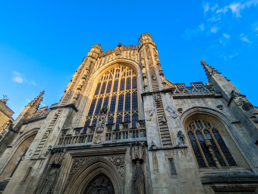 Bath Abbey looming from a low angle, with Medieval detailing piercing the bright blue sky.