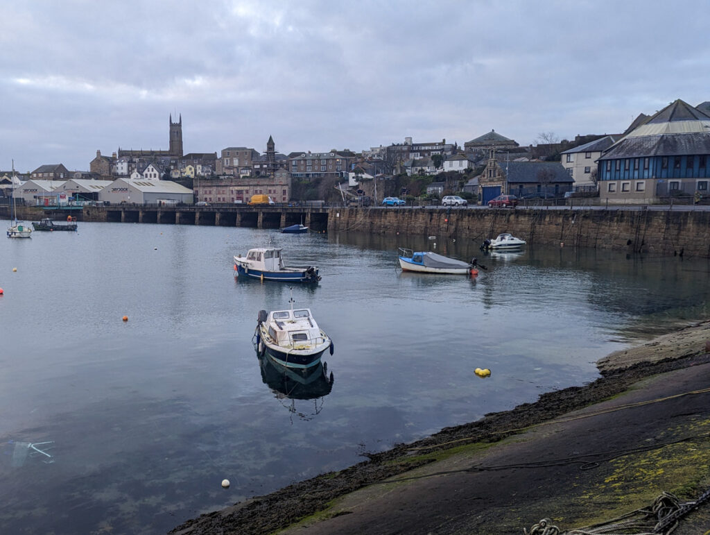 Penzance harbour on a cloudy January day, with boats in the harbour and historic buildings lined on the skyline.
