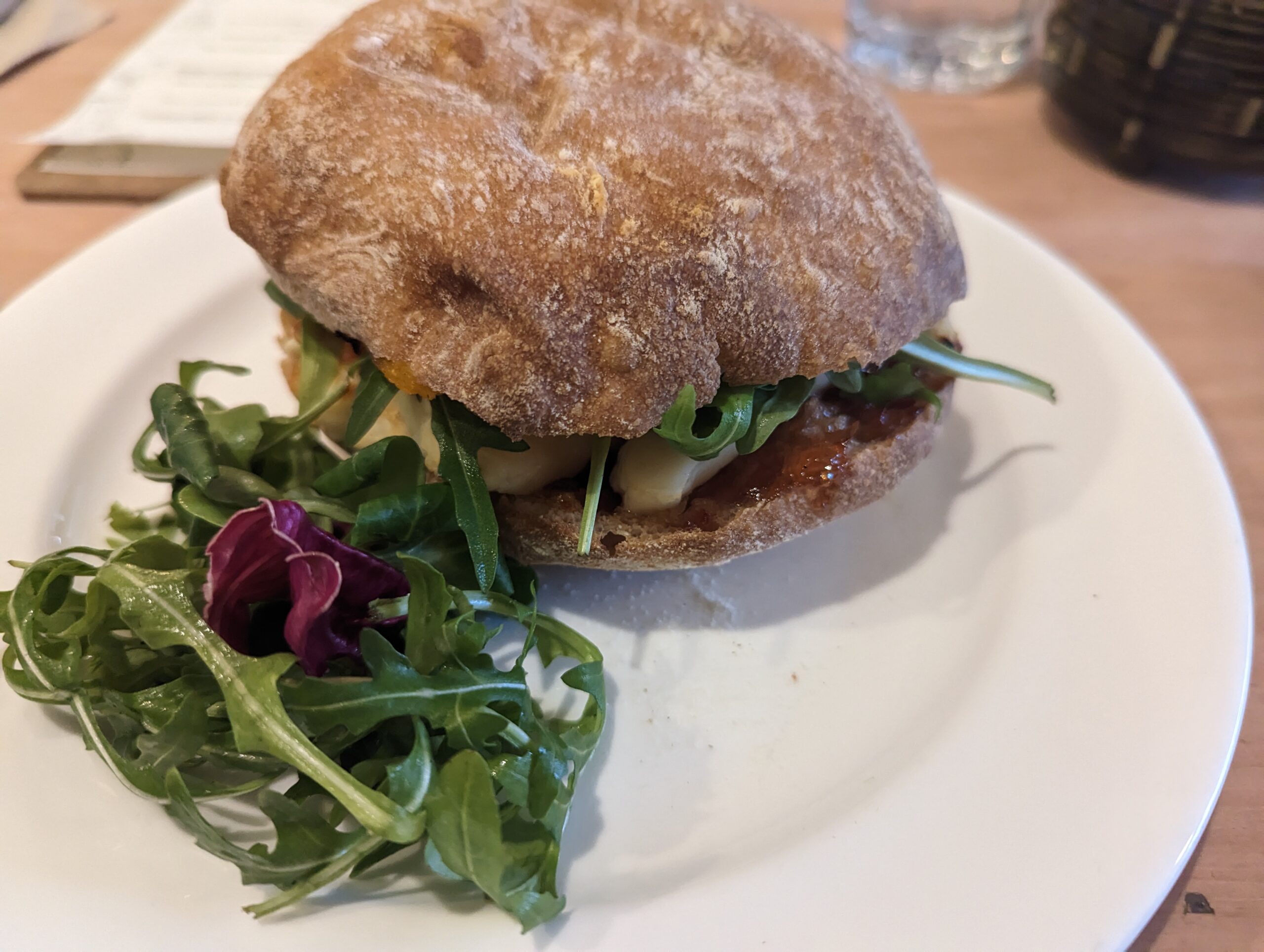 A ciabatta at the honey pot cafe with rocket, squash puree and halloumi on a white plate.