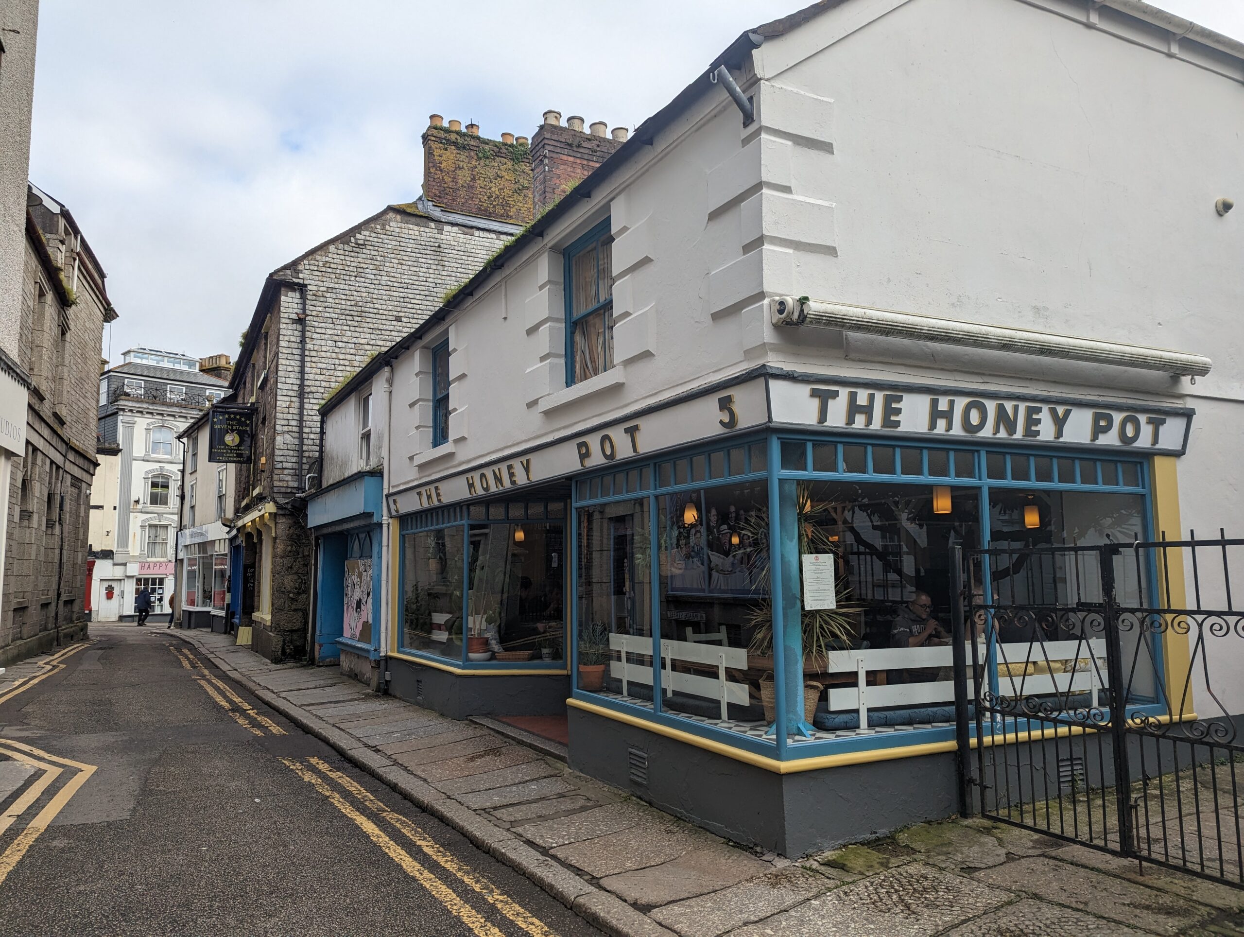 The honey pot cafe in Penzance. It's a shot of the corner of the street, with white building and blue lettering on the cafe. 