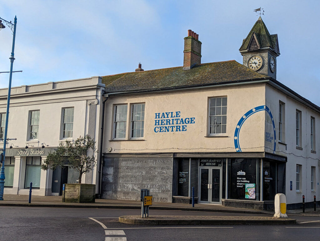 The Hayle Heritage Centre, which is located in a cream-coloured building in the heart of the town centre, with blue lettering and the brilliantly blue sky above it.