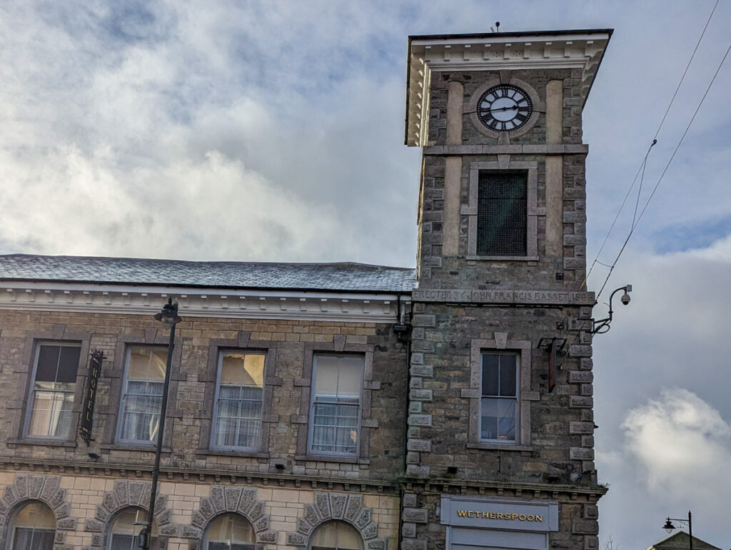 The historic building of Wetherspoons in Camborne, with a clock tower. It's an 18th century building and there's cloud in the sky.