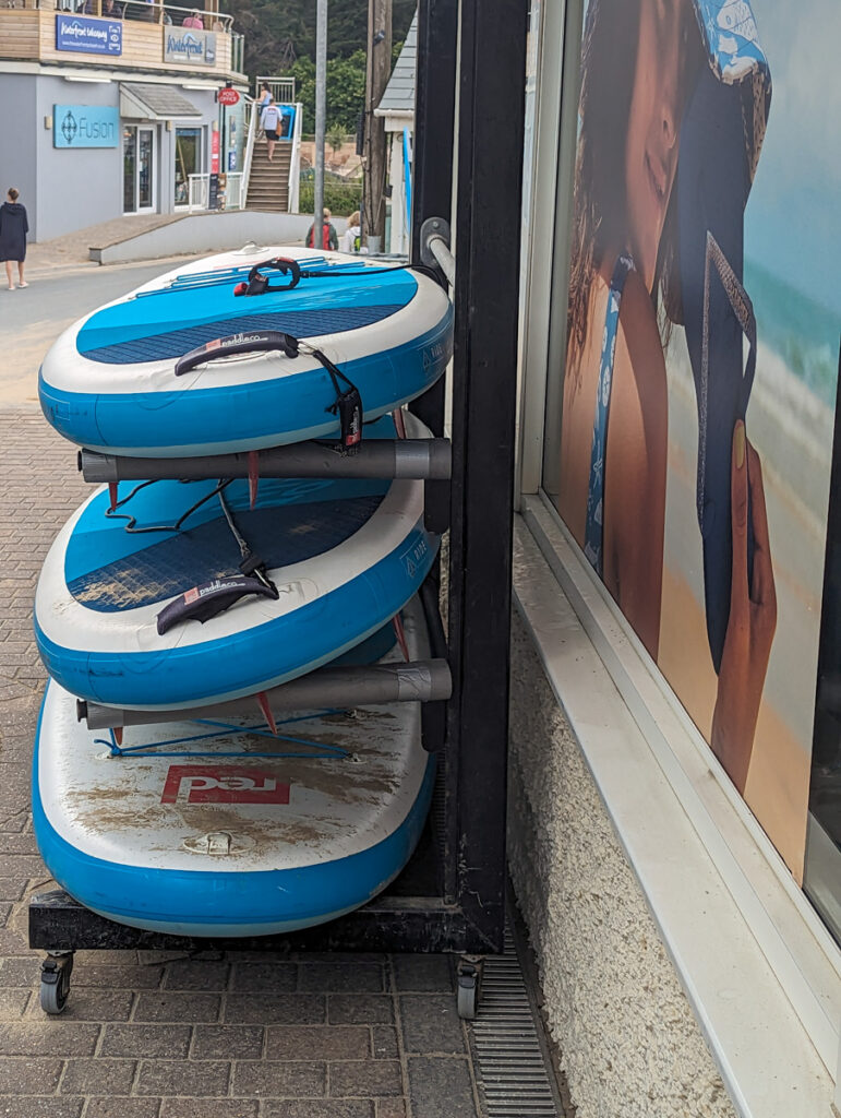 Stand up paddleboards for hire in Polzeath. Boards are stacked up one on another. 