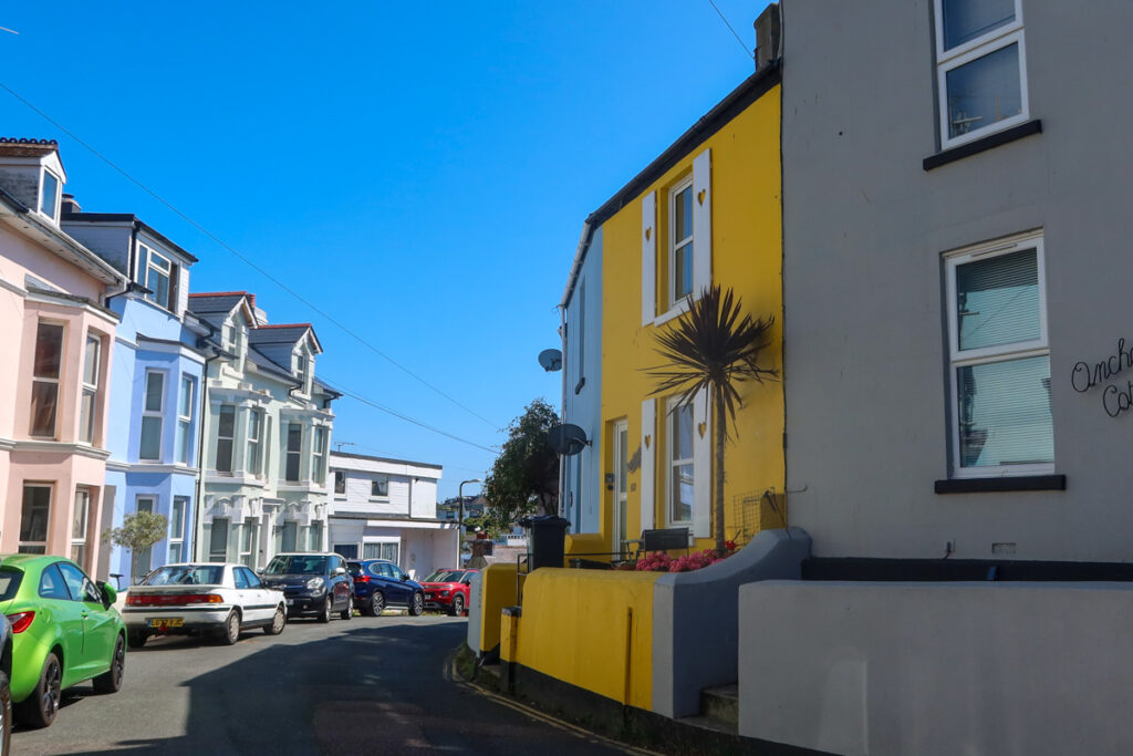 Bright yellow house on one side and pastel coloured buildings on another in Brixham.