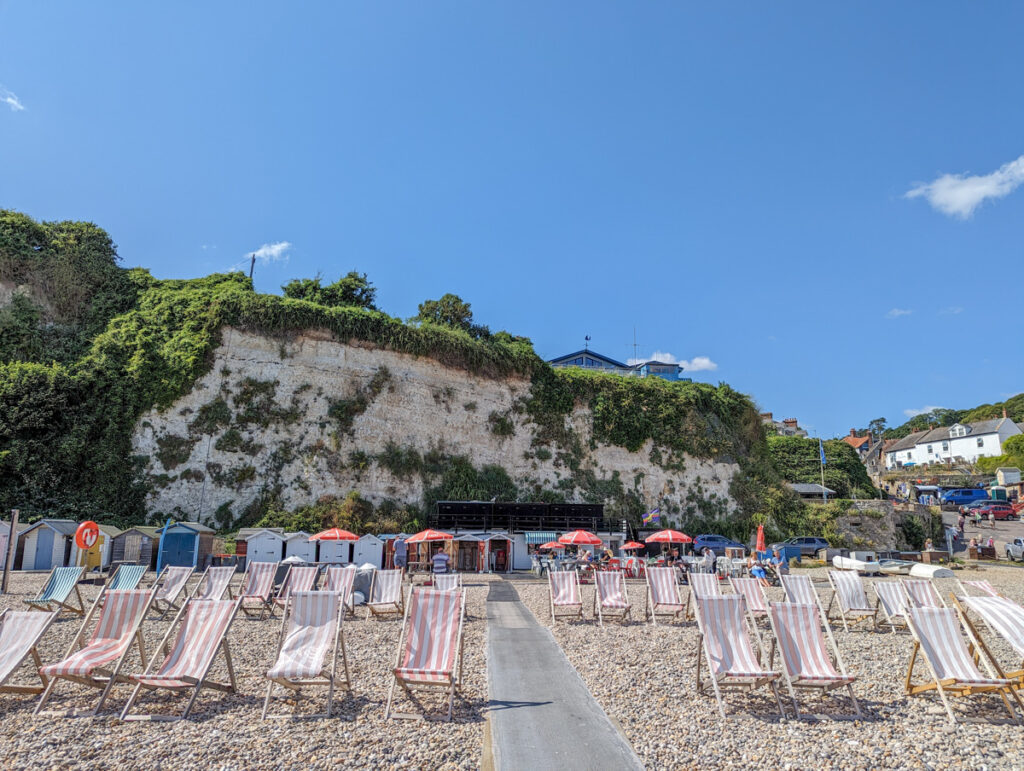 Pink and white striped deckchairs situated on the pebbles of the beach.