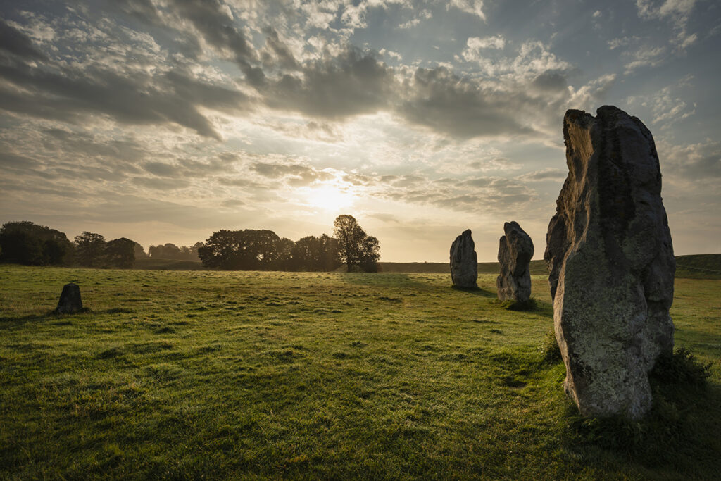 Beautiful Summer sunrise landscape of Neolithic standing stones in English countryside with gorgeous light with background mist
