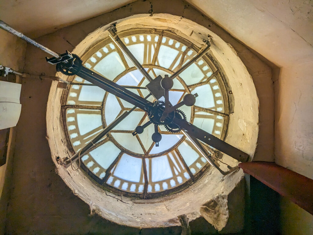 Inner workings of an antique tower clock with visible gears and hands, set against the translucent face and casting shadows, exemplifying historical timekeeping.