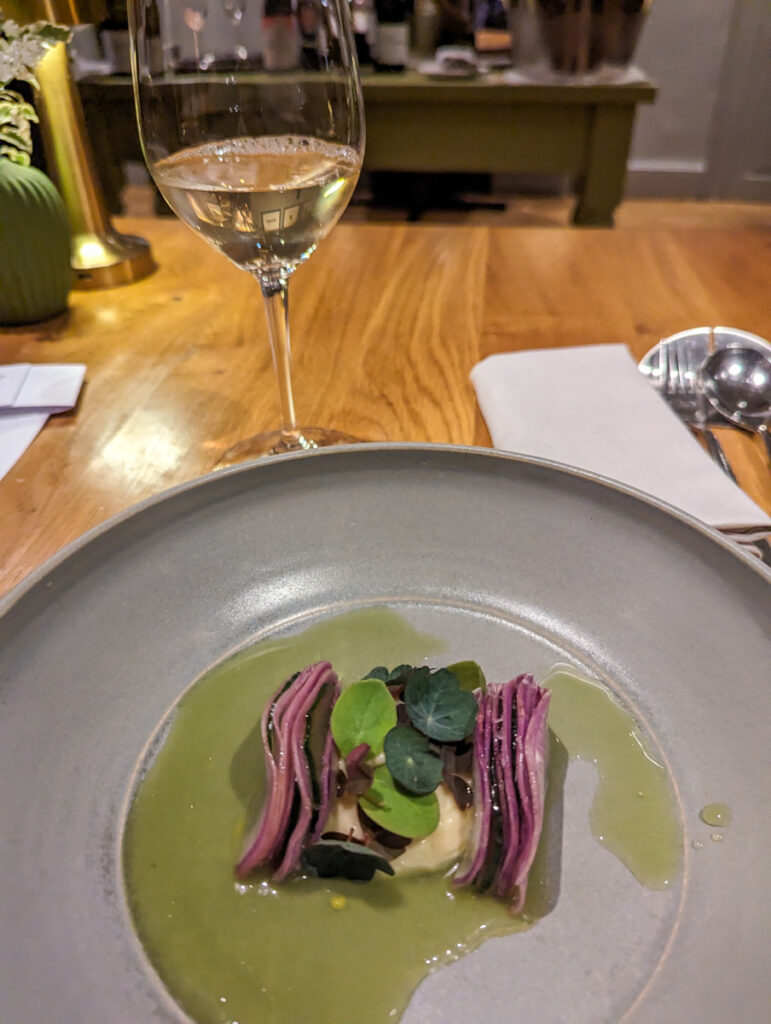 Elegant dining experience featuring a glass of white wine and a dish with purple artichoke hearts on a grey plate, atop a wooden table