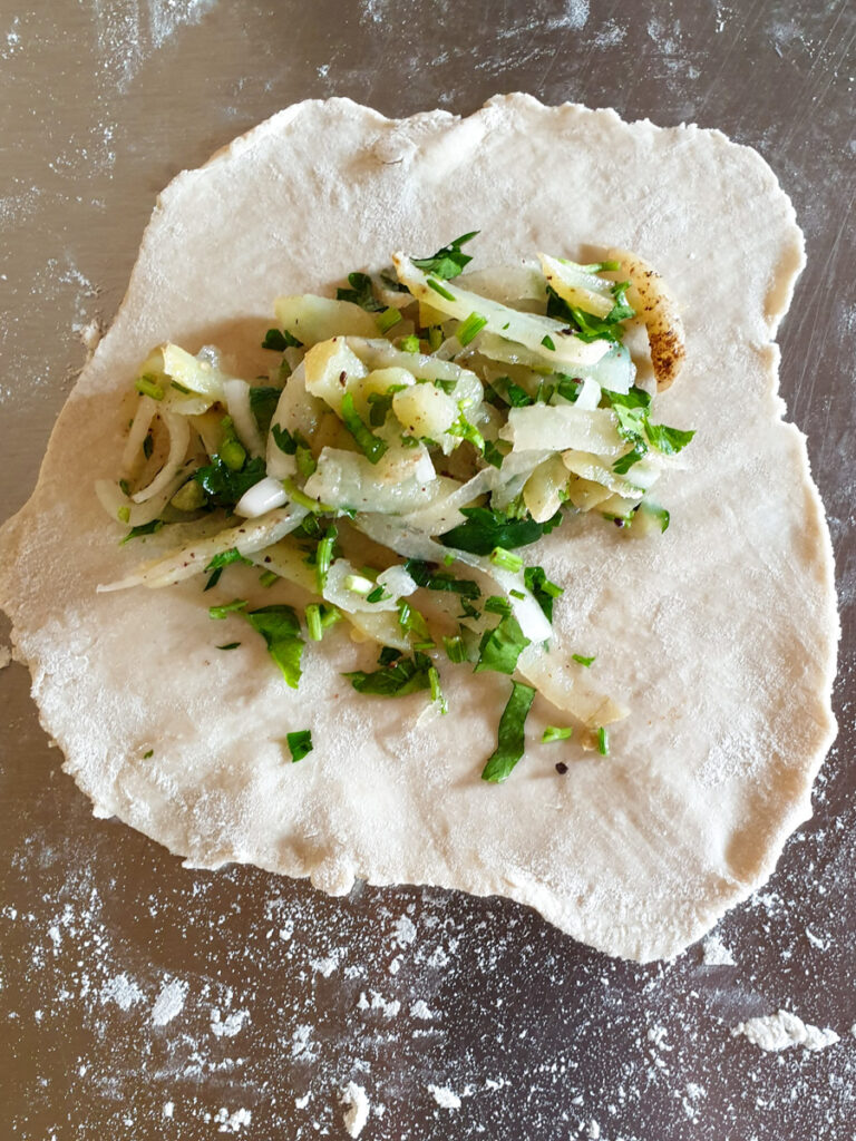 A Mexican pasty being made, showing the inner ingredients of onion, potato and cilantro