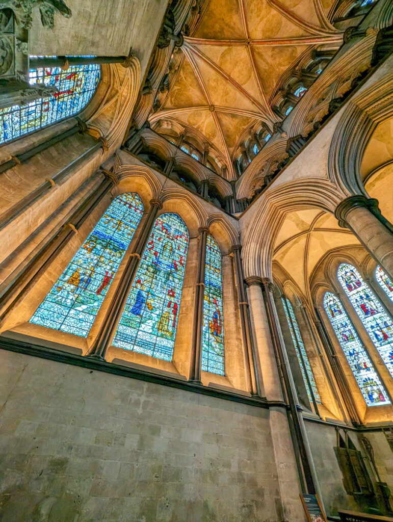 A set of three large, arched stained glass windows within the cathedral, each filled with deep blues and other vivid colors, illustrating religious narratives in intricate detail.