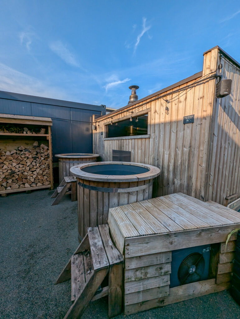 A warm, inviting hot tub surrounded by a wooden fence, with two chimneys extending above, under a clear sky with a few plants adding a touch of greenery.